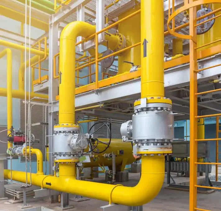 Industrial facility with large yellow gas pipes, metal valves, and platforms, showing part of a pipeline system with safety features and structural supports.